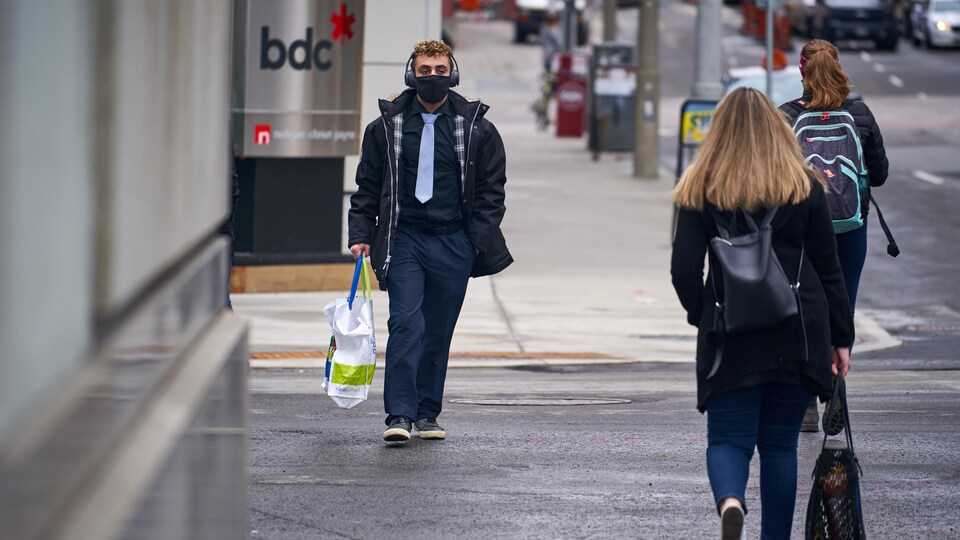 Un homme marche dans la rue avec un masque sur le visage.