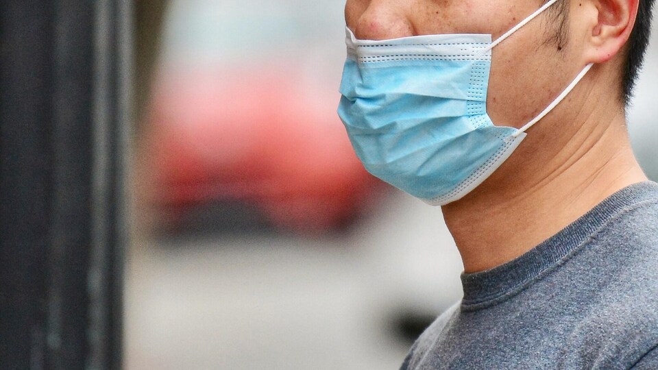 Un passant le visage couvert d'un masque bleu.