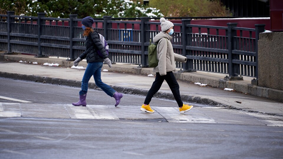 Deux personnes avec des masques se croisent en traversant la rue.