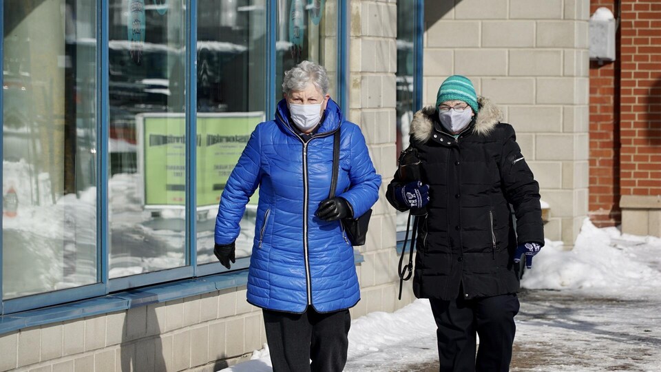 Deux personnes marchent sur un trottoir et portent un masque.