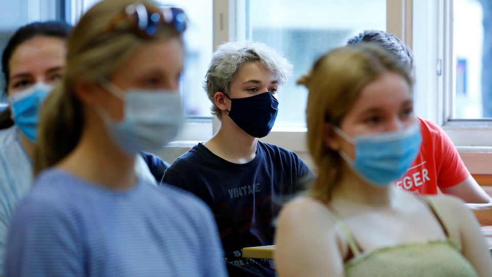 Des adolescents sont assis à leur pupitre dans une salle de classe. Ils portent tous un masque non médical sur le visage.