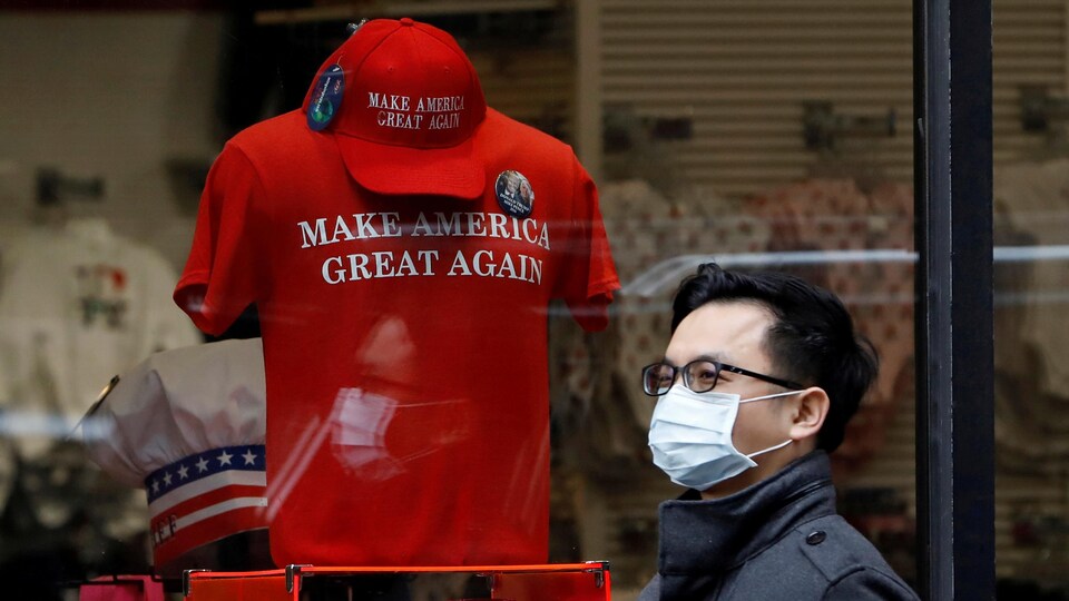 Un homme portant un masque chirurgical passe devant une vitrine où l'on vend un chandail « Make America Great Again ».