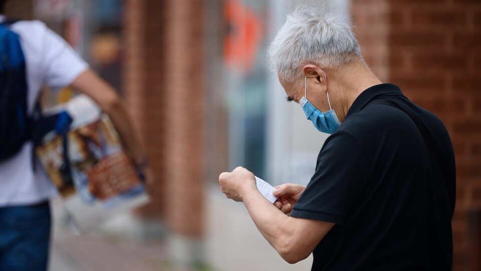 Un homme qui porte un masque examine son coupon de caisse à la sortie d'un commerce.