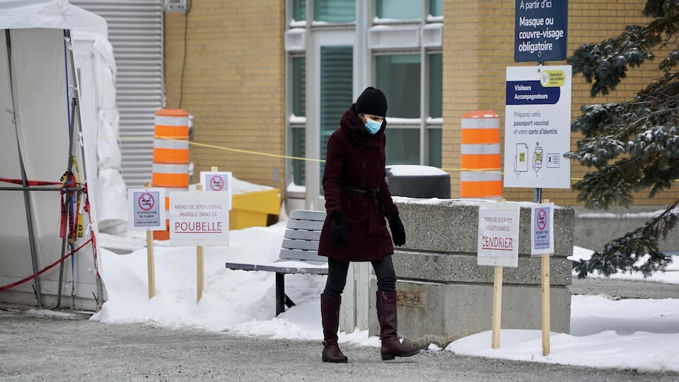 Une personne qui porte un masque marche sur un trottoir près de l'entrée d'un hôpital.