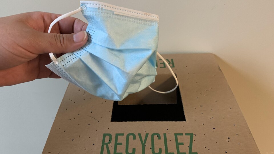 Une femme dépose un masque d'intervention dans une boîte de recyclage prévu à cet effet.
