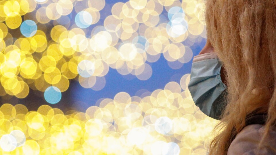 Une personne portant un masque devant des lumières de Noël jaunes scintillantes le 23 décembre 2020 à Rome, en Italie.