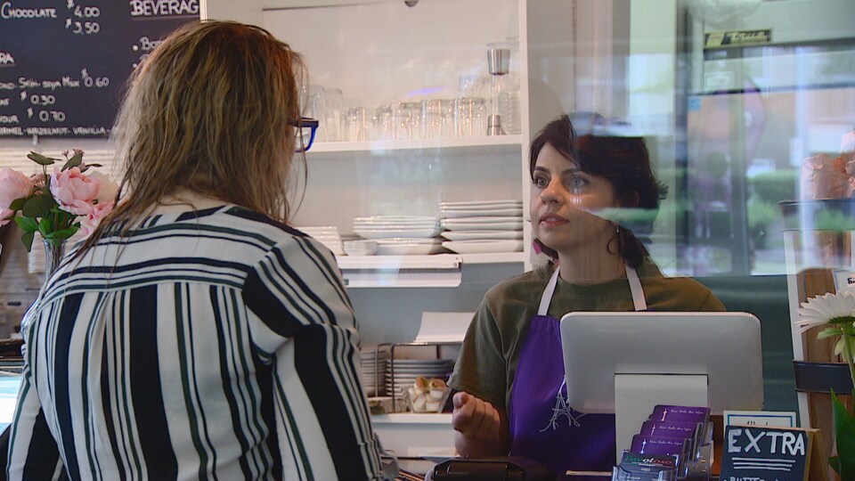 Une employée parle à un client à sa caisse, équipée d'un plexiglas.