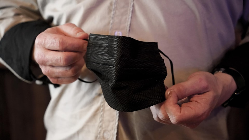 Un homme tient dans ses mains un masque sanitaire noir.