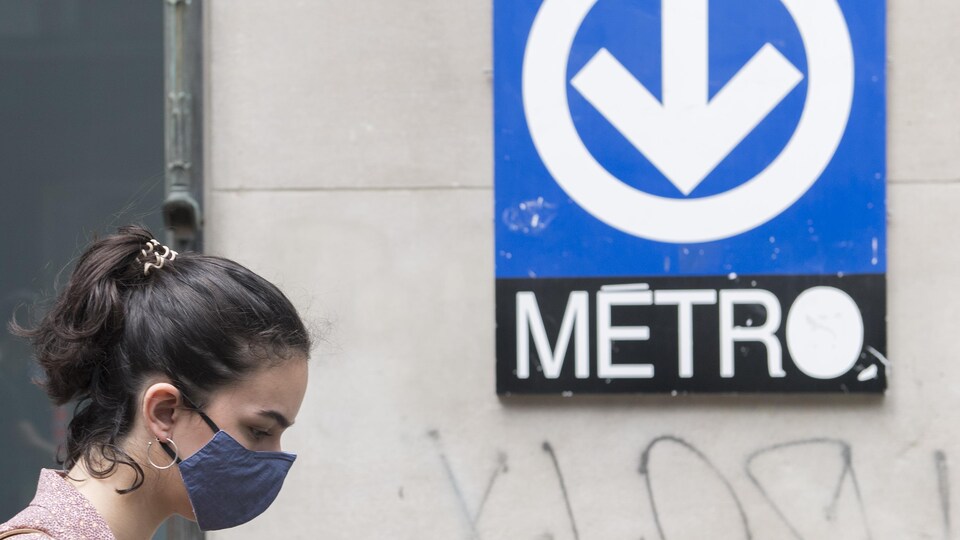 Une femme porte un masque devant une affiche du métro.