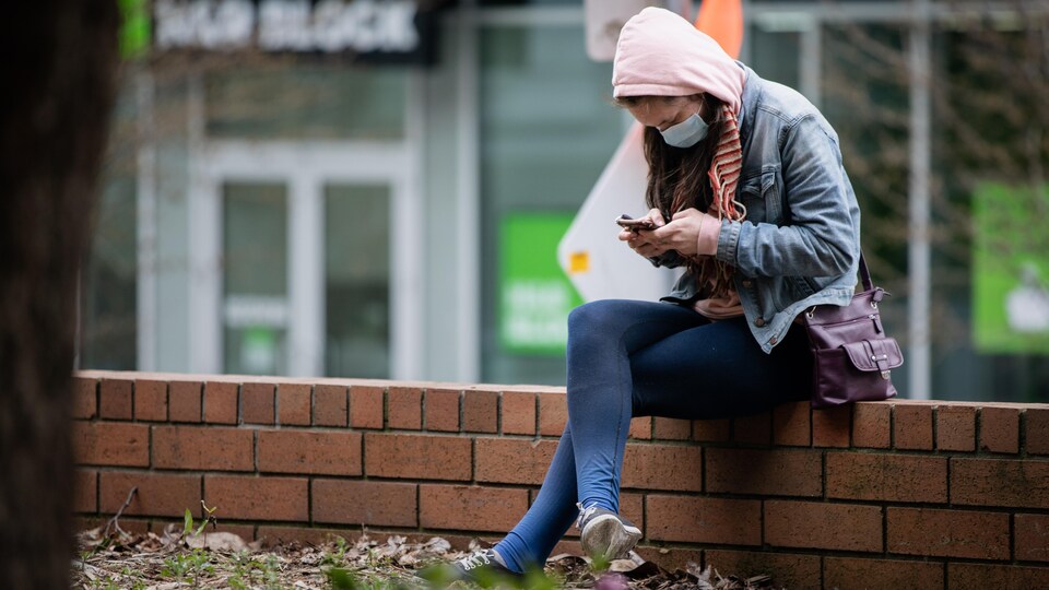 Une femme assise sur un muret est penchée sur son téléphone.