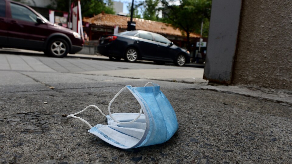 Un vieux masque jetable traîne sur le trottoir.