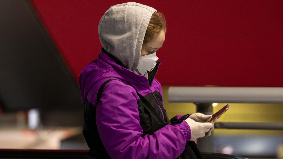 Une femme portant un masque se promène à Madrid en tenant son téléphone.