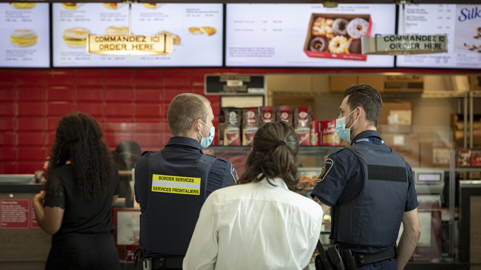 Des clients portant un masque en file dans une succursale Tim Hortons à l'aéroport Pearson.
