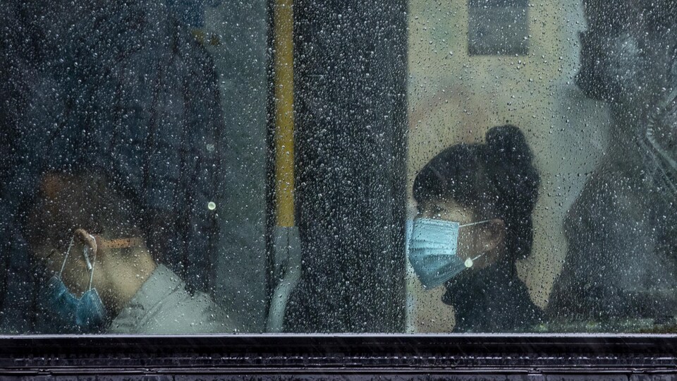 Des personnes, que l'on aperçoit à travers une fenêtre embuée par la pluie, portent un masque dans un autobus de Vancouver. 