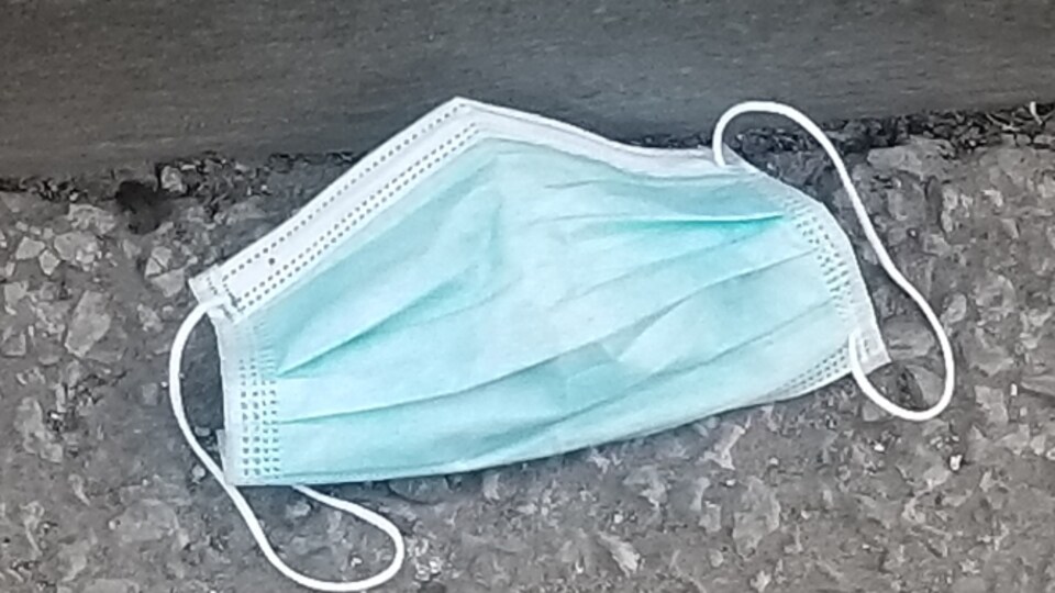 Un masque chirurgical usagé a été jeté par terre, sur l'asphalte.