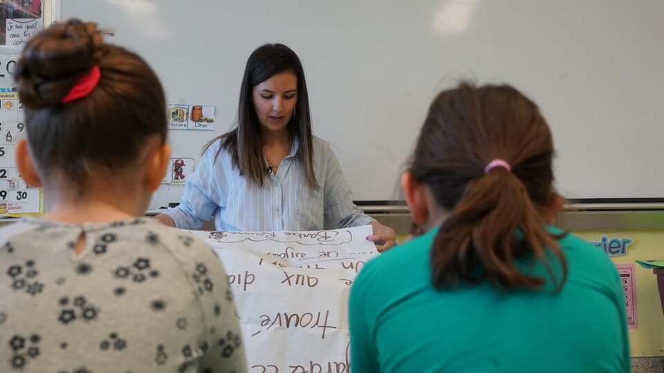 Une enseignante dans une salle de classe présente une activité d'écriture à deux filles.