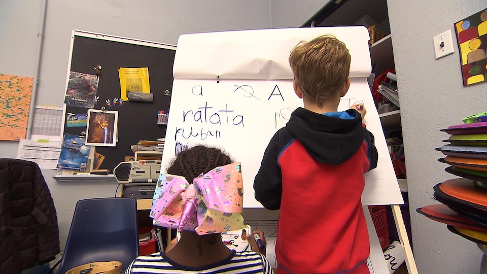 Une fillette et un garçon écrivent sur un tableau des mots. 
