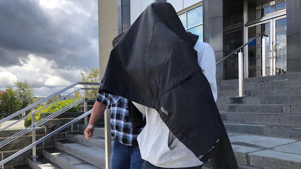 Un homme a mis son manteau sur sa tête pour descendre les marches du palais de justice de Rouyn-Noranda.