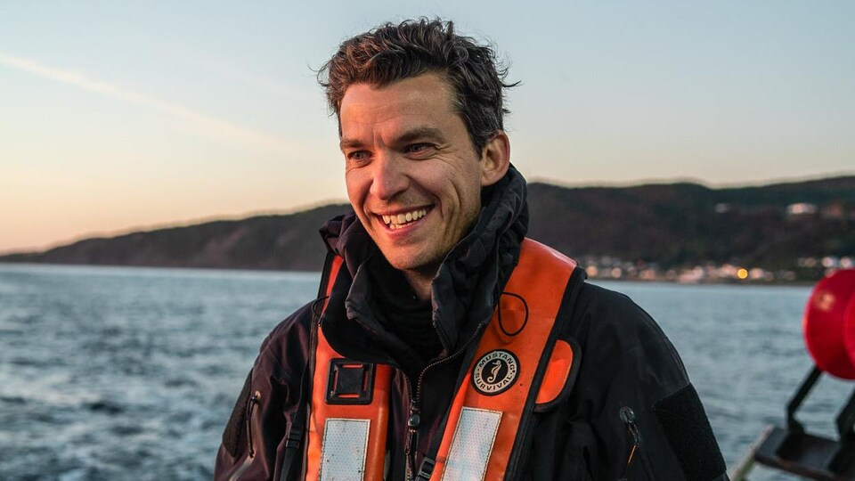 Le photographe Mathieu Dupuis sur un bateau de pêche, caméra autour du cou.