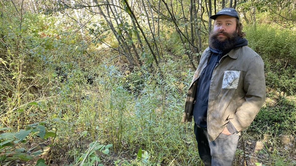 Un homme barbu se tient debout sur les lieux de son travail dans un parc entouré de saules de l'intérieur.