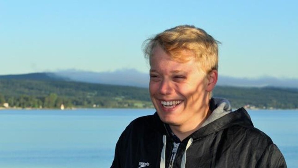 Un jeune homme souriant pose devant un grand plan d'eau.