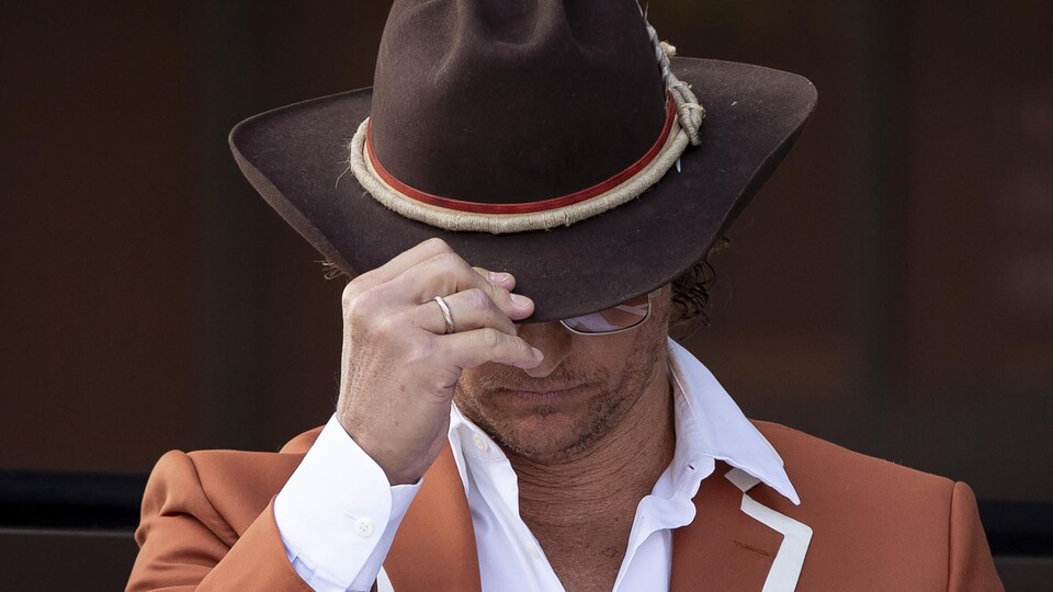 Matthew McConaughey, stooped, holding his cowboy hat.