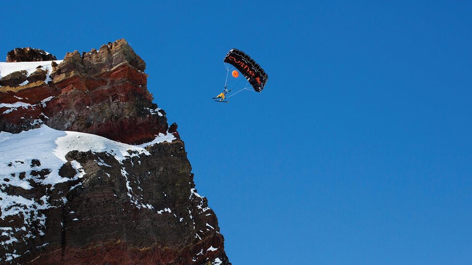 un homme faisant du ski-BASE jump, en parachute.