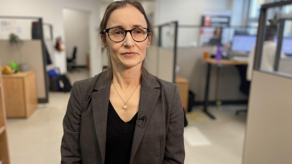 Une femme portant des lunettes se tient debout dans un espace de bureaux.