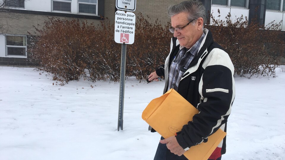 Un accusé marche vers sa voiture à la sortie du palais de justice de Rouyn-Noranda, une enveloppe jaune à la main.