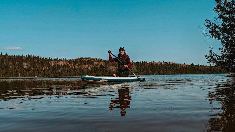 Une femme est assise sur une planche à Pagaie dans le milieu d'un lac.