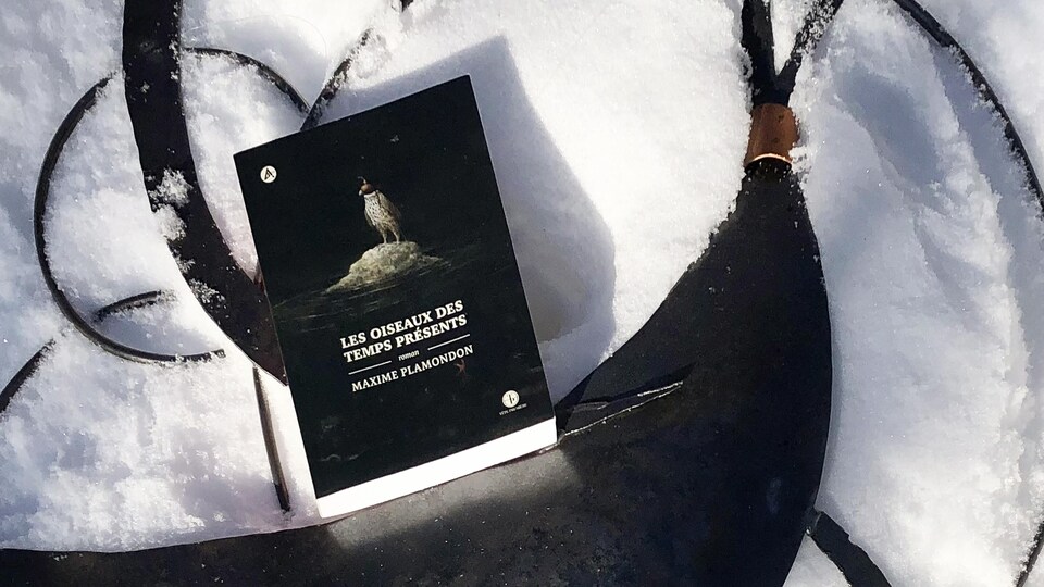 Le livre est déposé sur une sculpture de métal représentant un oiseau, sur fond de neige.