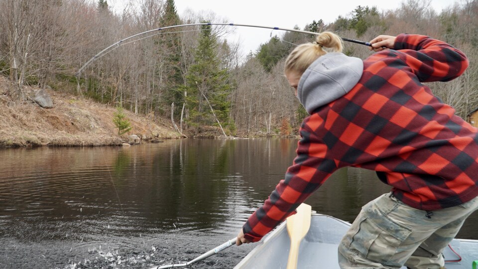 Un homme en chemise à carreau sort avec une puise une truite d'un lac.