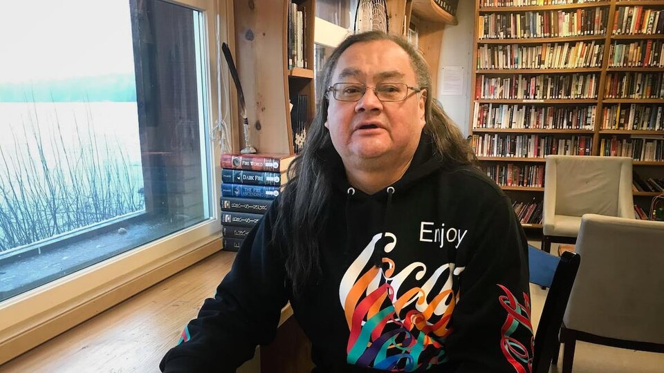 Plan moyen de Maxwell Johnson assis devant des étagères de livres.