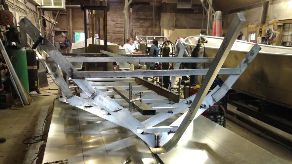 The metal structure of a boat rests on an assembly line.