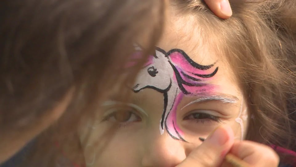 Gros plan sur une main qui peint une licorne sur le front d'une jeune fille.
