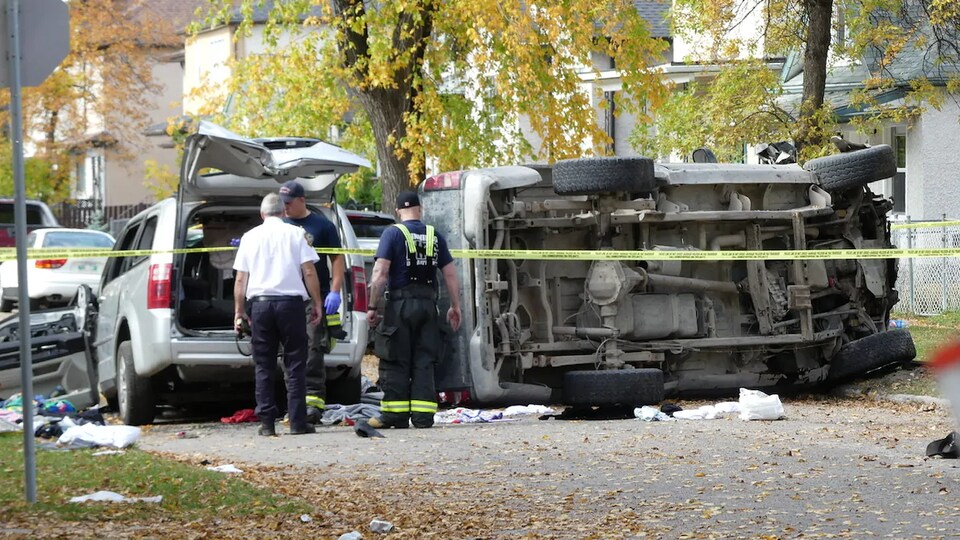 Des policiers observent un camion renversé et une camionnette endommagée dans une rue bordée par des arbres, le 26 septembre 2020.