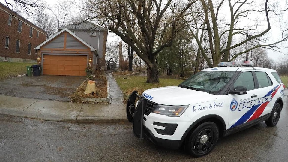 Photo d'un véhicule de police devant le garage d'une maison grise à deux étages.