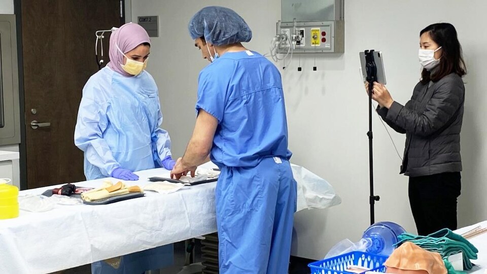 Deux médecins, qui sont filmés par une femme, prennent des instruments chirurgicaux.