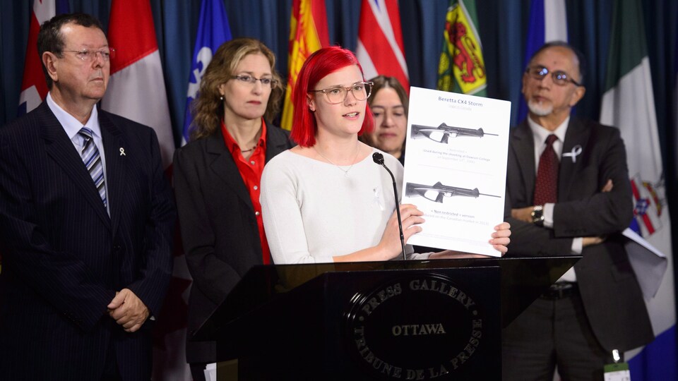 Une jeune fille aux cheveux rouges tient une image d'armes à feu lors d'une conférence de presse.