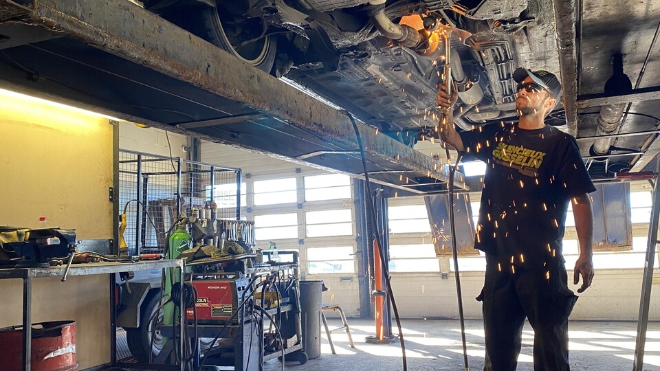 Un homme équipé d'un chalumeau répare un véhicule dans un garage. 