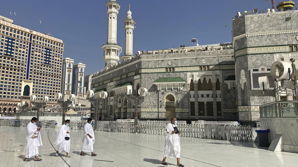 Des hommes portant le couvre-visage marchent à proximité de la Grande Mosquée, en plein jour.
