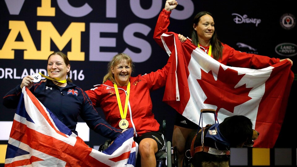 Christine Gauthier, assise dans un fauteuil roulant, célèbre en compagnie de deux autres athlètes.