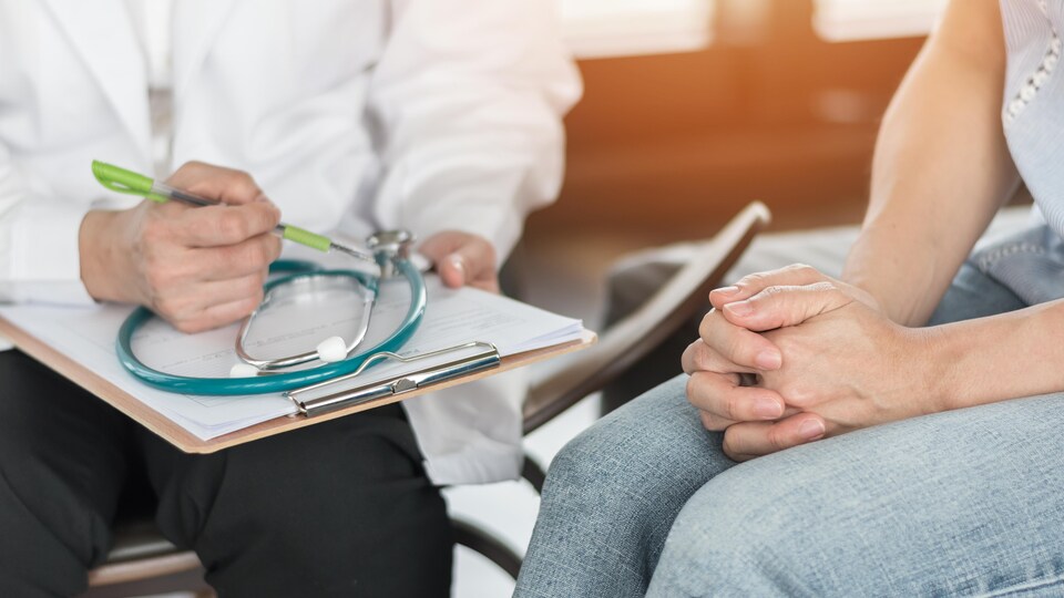 Une femme consulte un médecin, qui prend des notes.