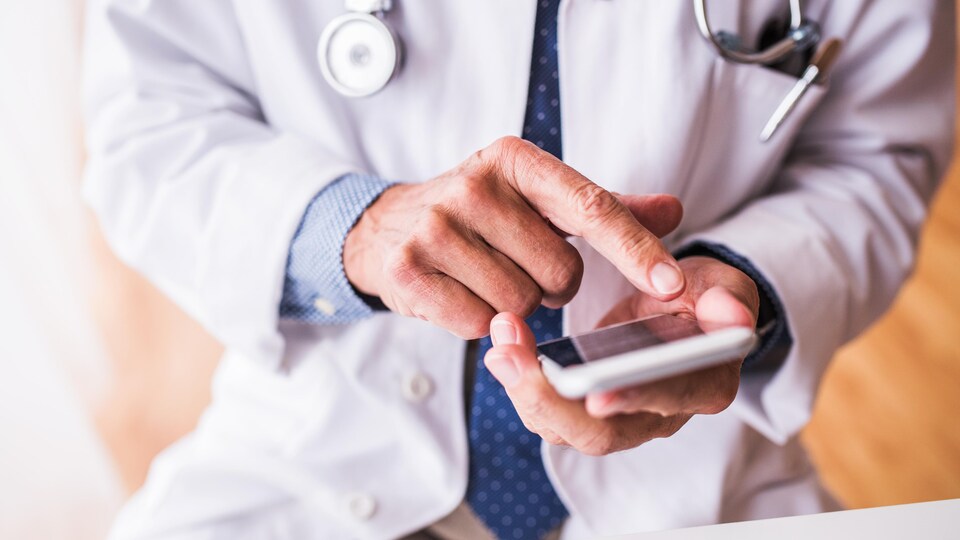 Un médecin tape sur l'écran de son téléphone cellulaire.