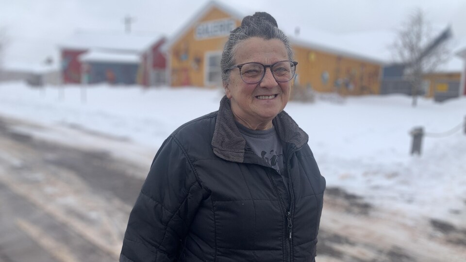 Marcelle Desroches se tient debout devant des édifices entourés de neige.  Elle sourit.