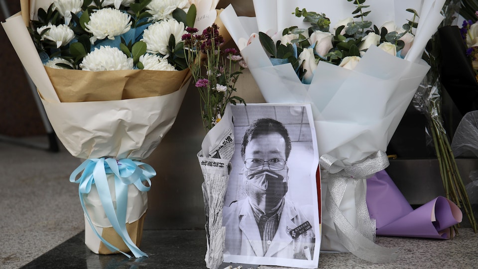 Des bouquets de fleurs près de la photo du jeune médecin sont déposés sur le sol.