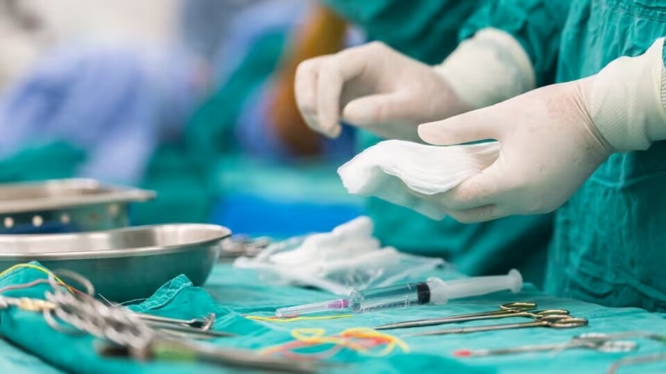Deux mains portant des gants chirurgicaux au-dessus d'instruments médicaux.