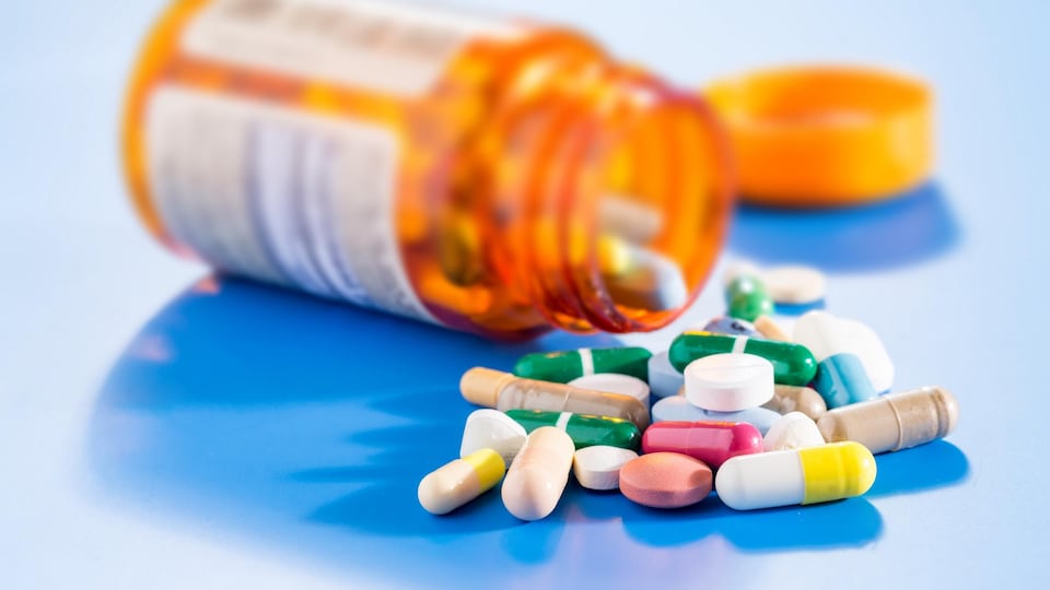 Des pilules de différentes couleurs à côté d'une bouteille de médicaments renversée.
