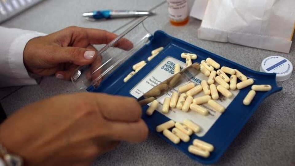 Un pharmacien compte des pilules beiges à l'aide d'une lame de métal.  