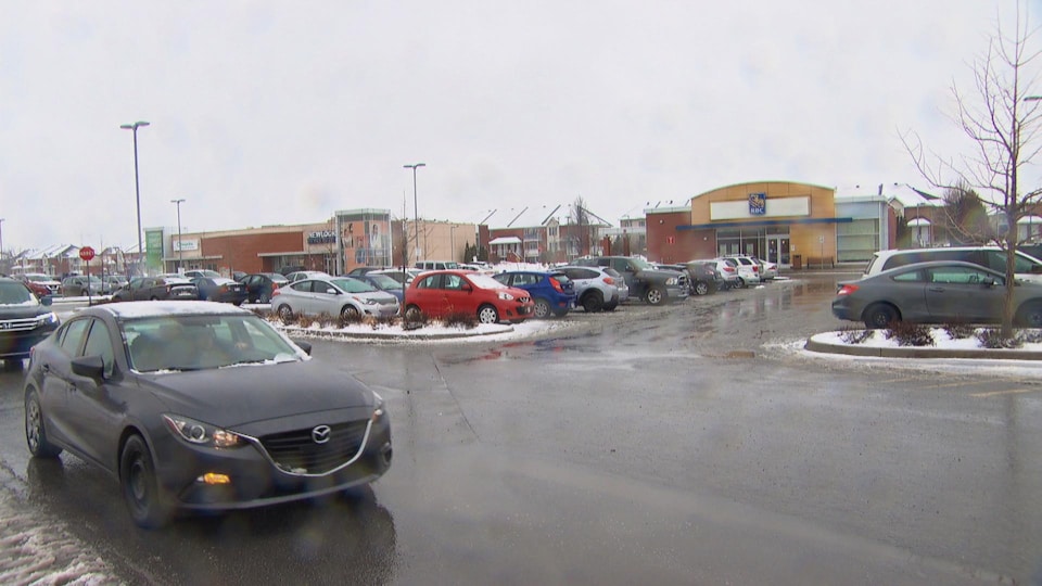 Plusieurs voitures dans un stationnement entouré de magasins.